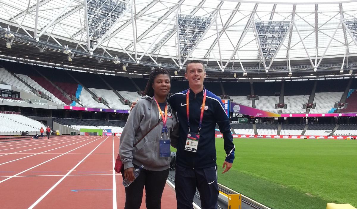 a female coach and male athlete stand together on the track at the London Stadium