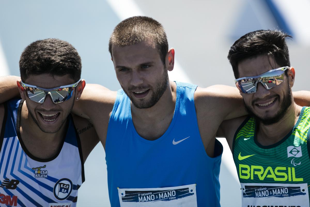 Petrucio Ferreira, Michal Derus, Yohansson Nascimento three male Para sprinters hug on the finish line