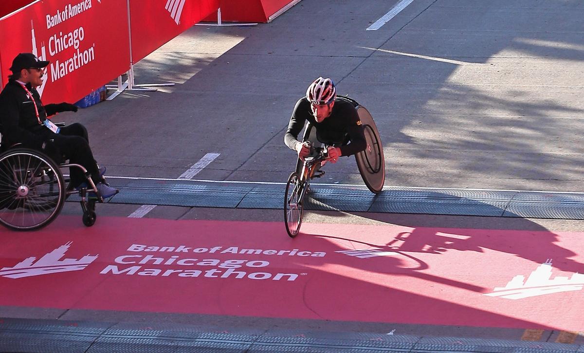 a male wheelchair racer crosses the finish line