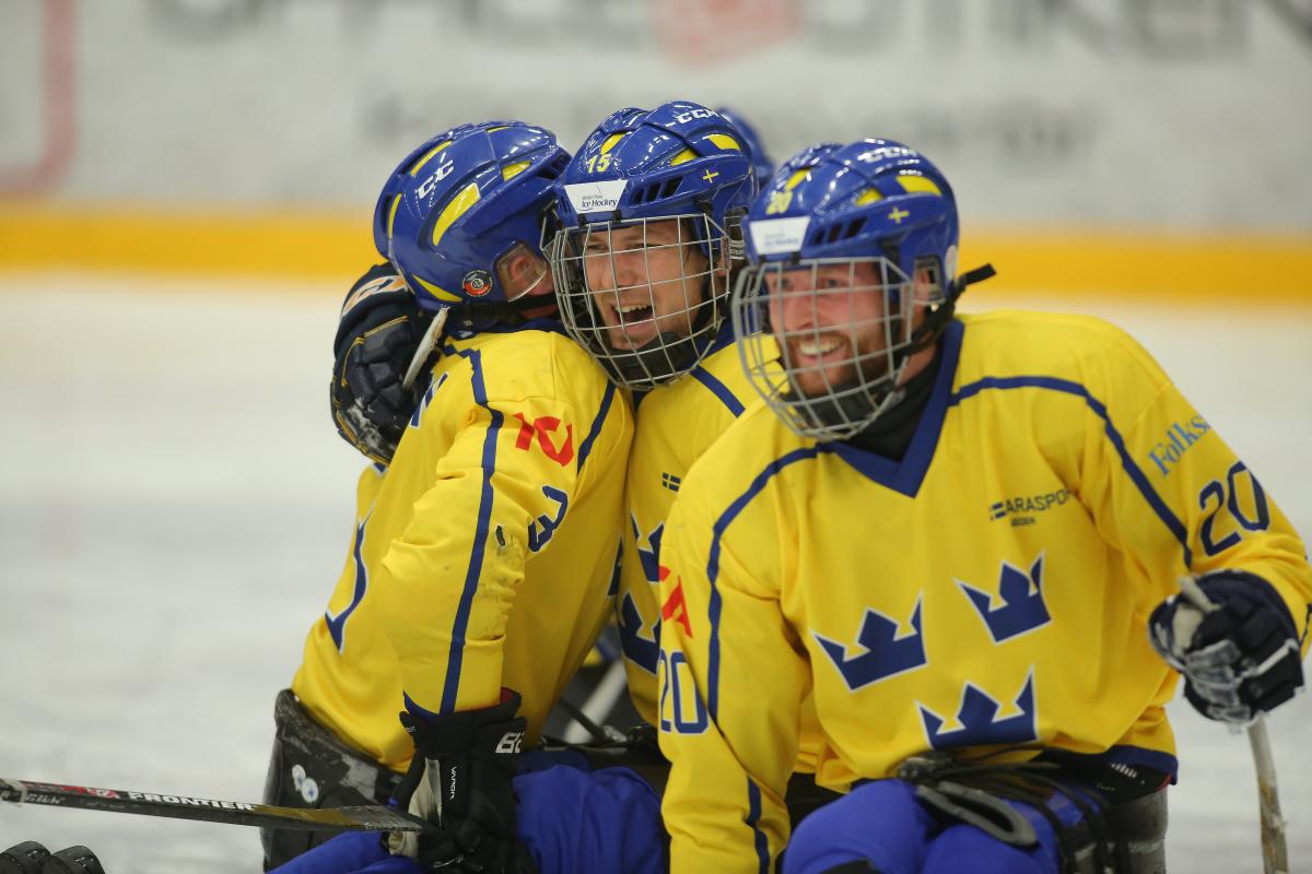 a group of Para ice hockey players hug on the ice