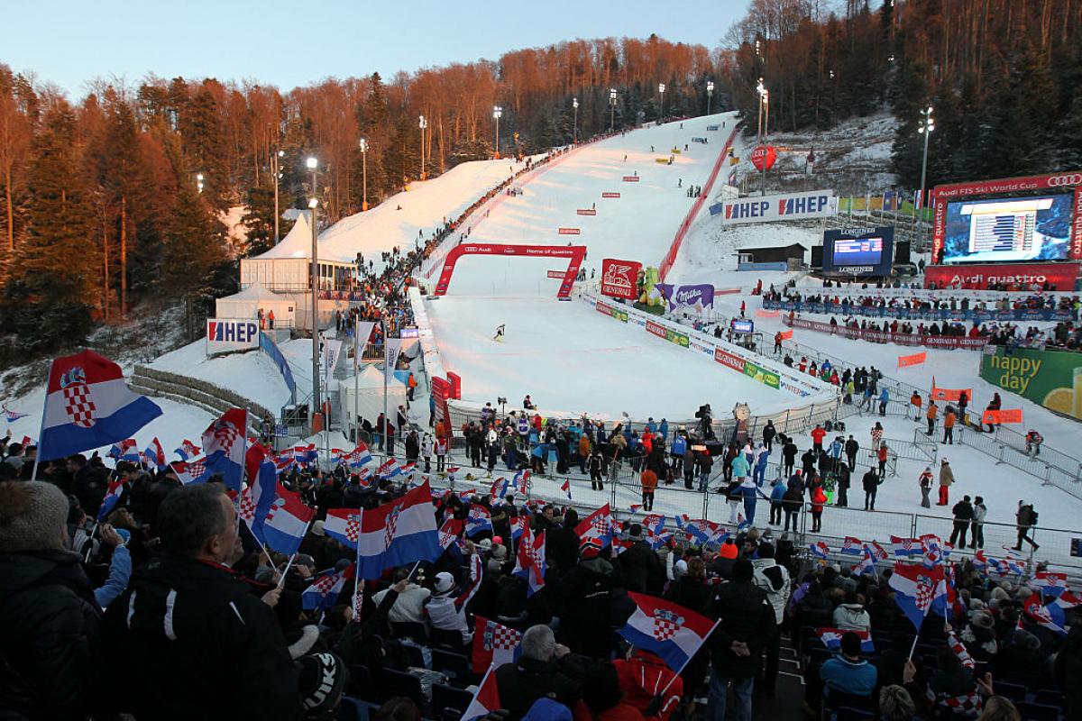 a crowd wait at the bottom of a ski run 