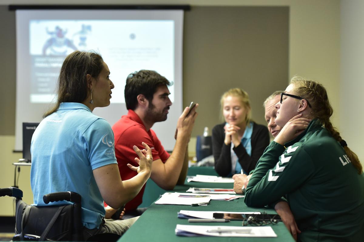 Four people talking in a meeting with a fifth person in the background