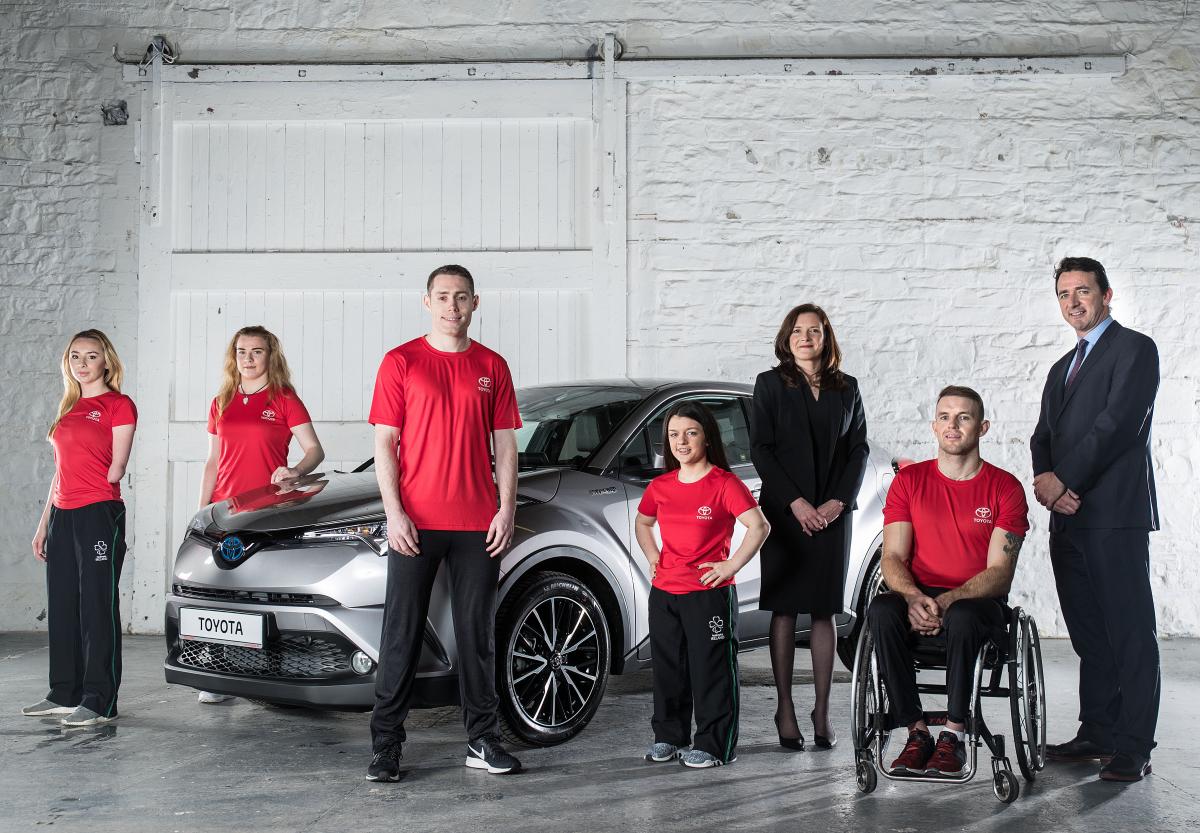 Seven people in front of a car. Six are standing and one is in a wheelchair 