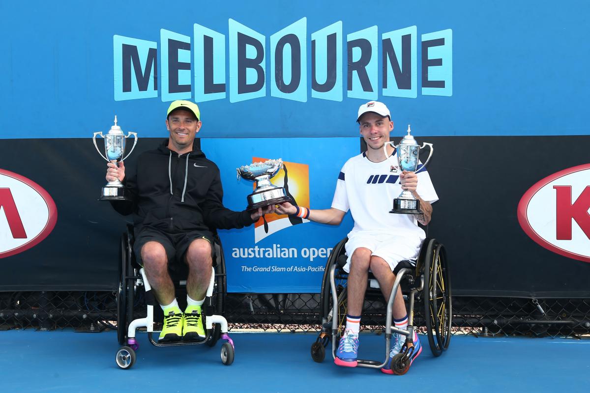 two male wheelchari tennis players hold up a trophy between them