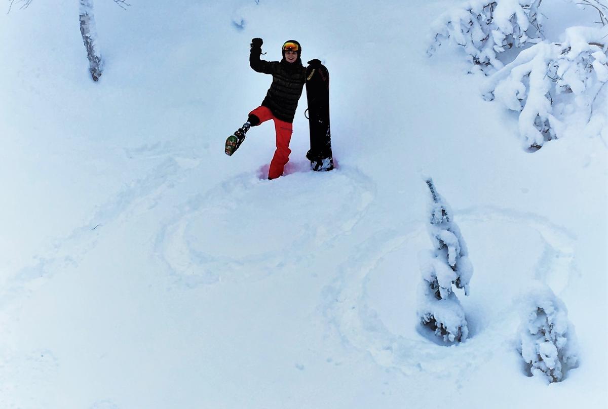 a male Para snowboarder stands on a '100' drawn in the snow