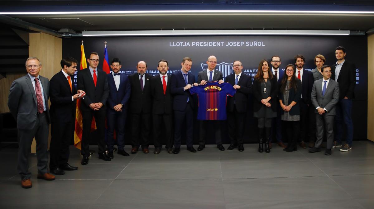 a group of men and women stand holding a Barcelona shirt