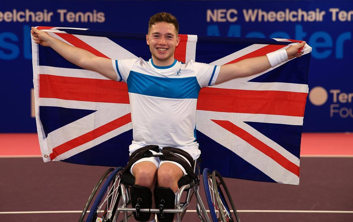 a male wheelchair tennis player holds up the Union Jack