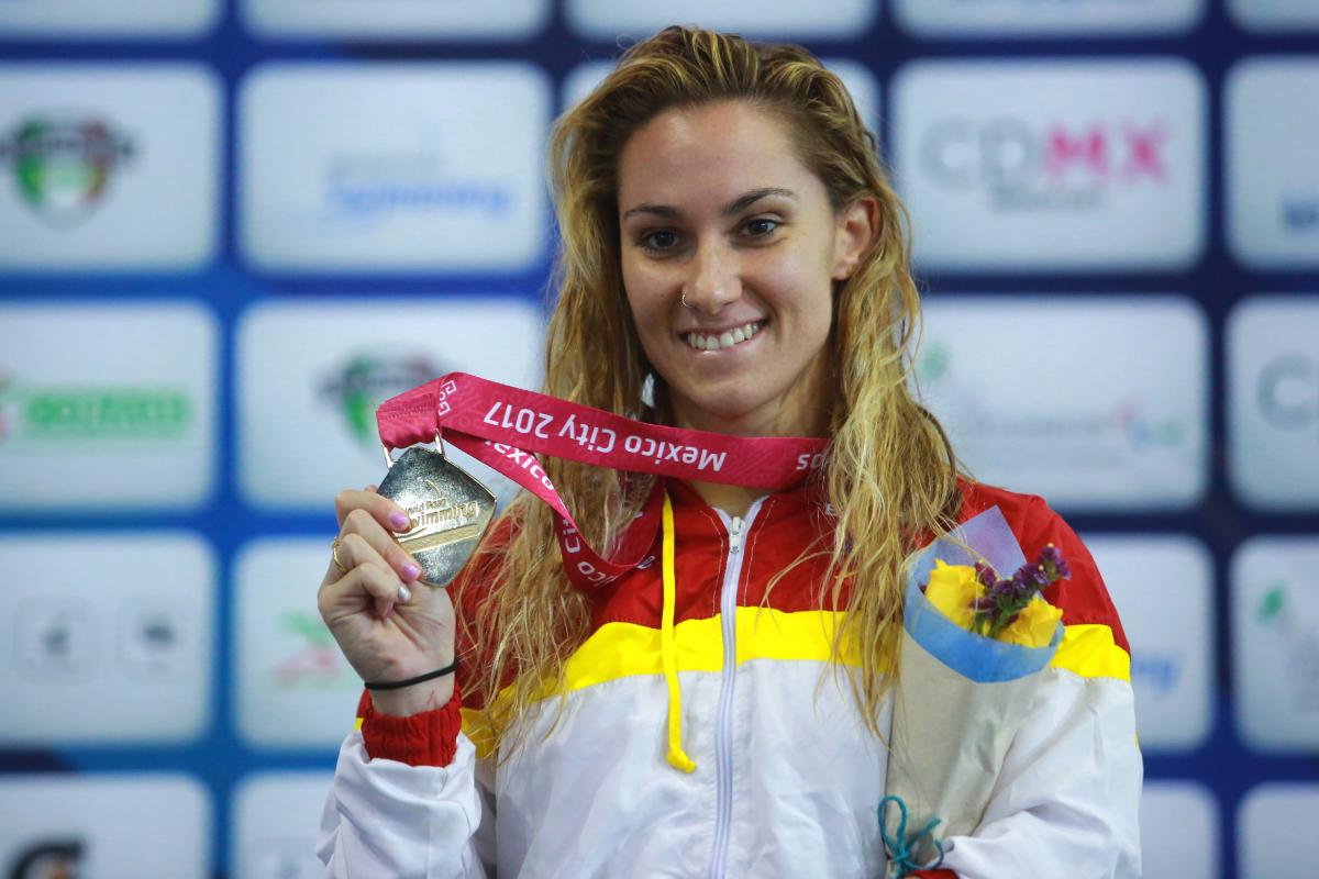 a female Para swimmer holds up her gold medal on the podium