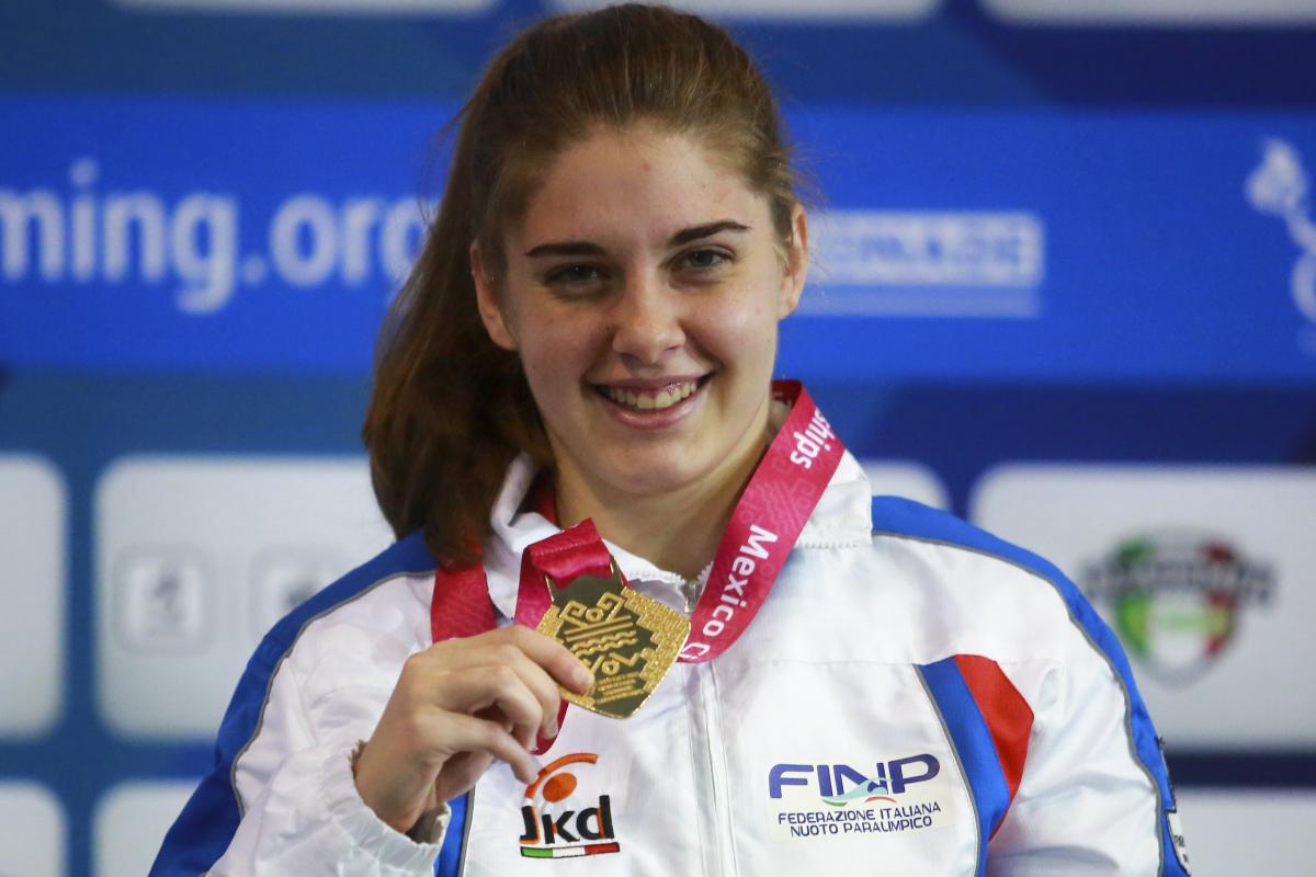 a female Para swimmer holds up her gold medal and smiles