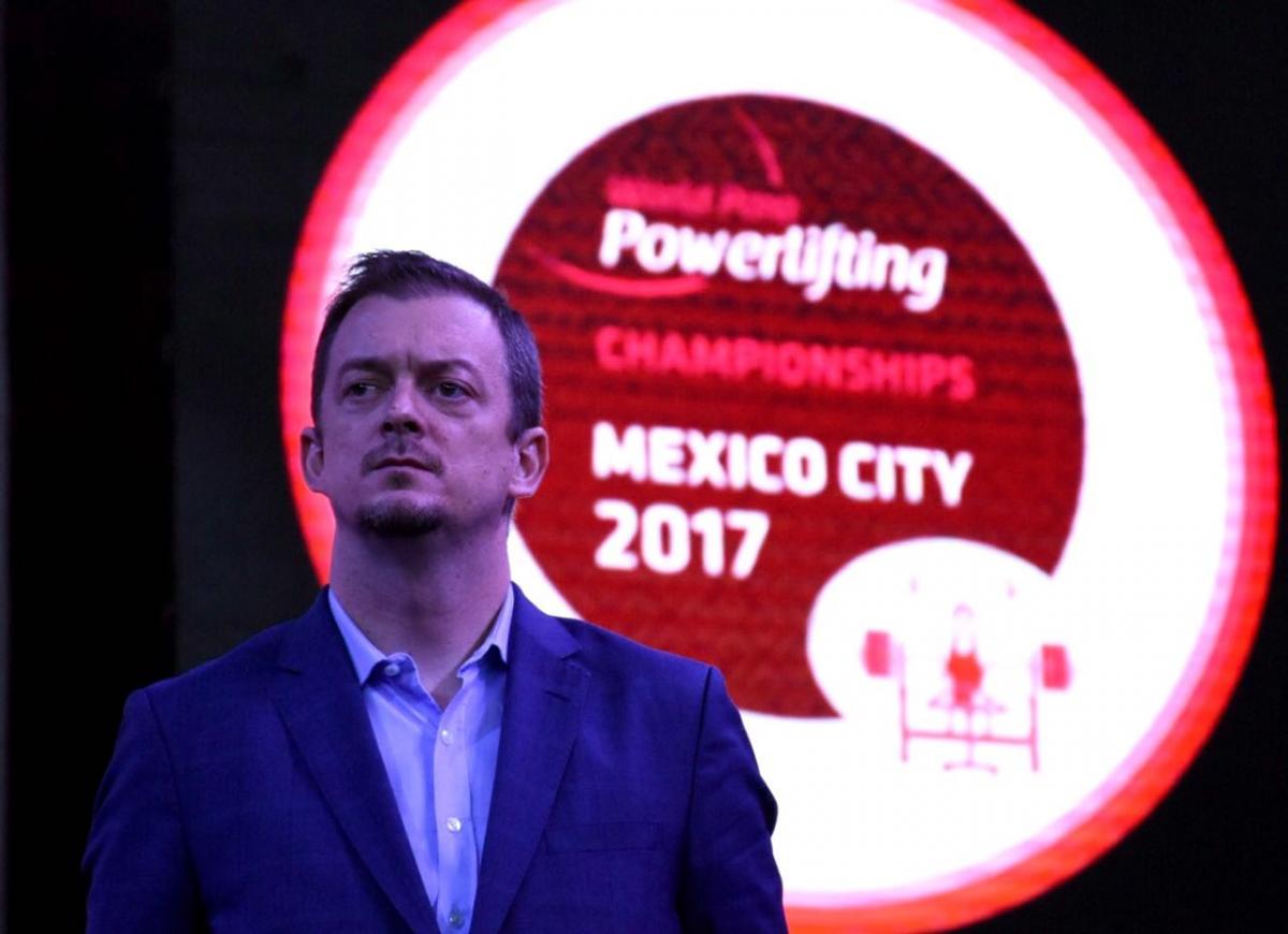 a man stands in front of the World Para Powerlifting emblem