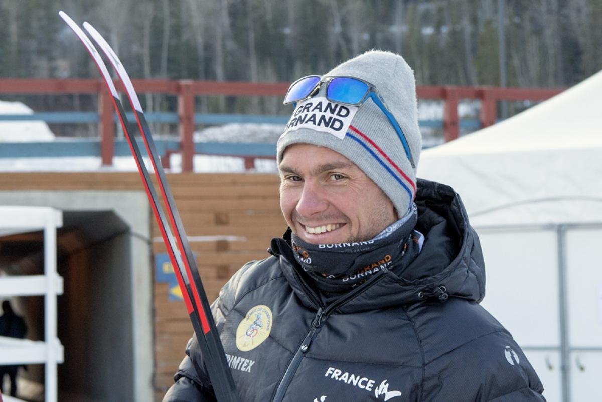 a male Para skier smiles at the camera while holding his skis