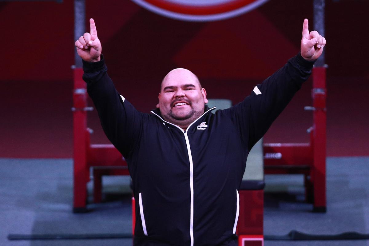 a male powerlifter raises his arms in celebration