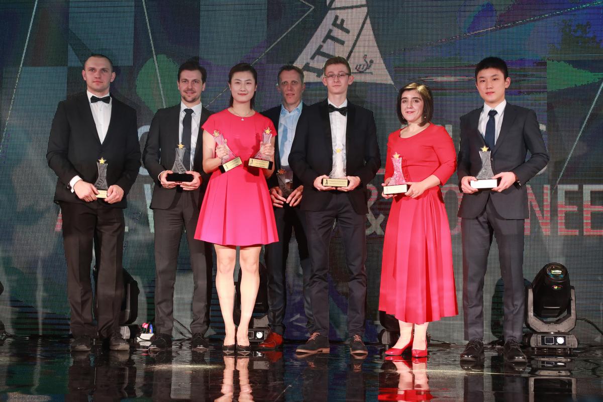 a group of men and women stand on stage with their trophies