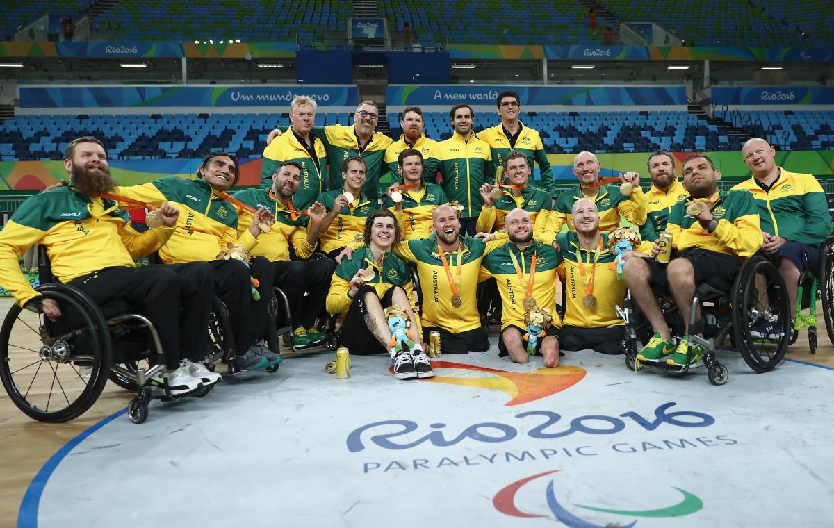 a group of wheelchair rugby players pose on the court with their medals