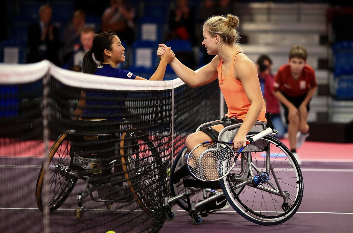 two female wheelchair tennis players shake hands over the net