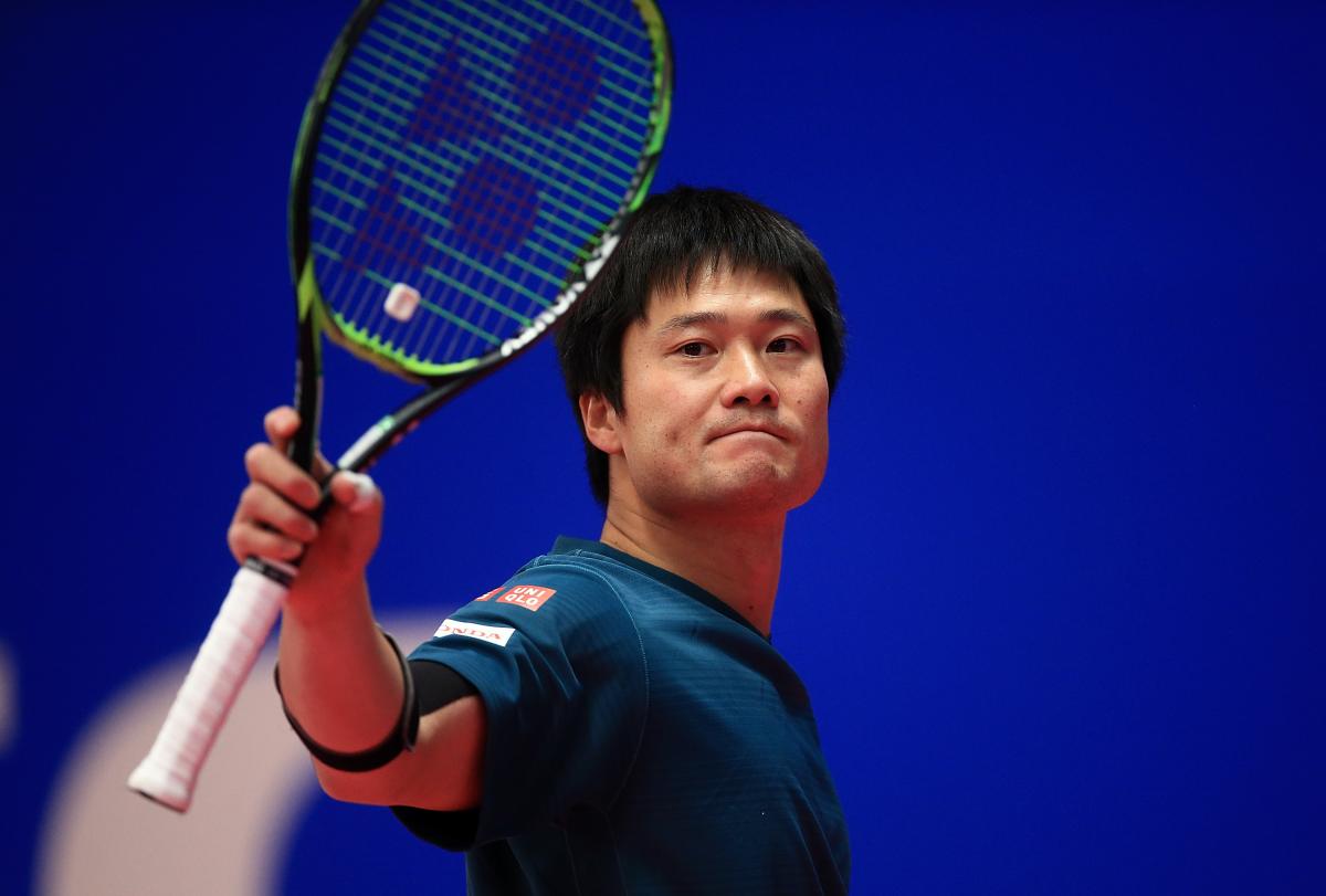 a male wheelchair tennis player holds up his racket 