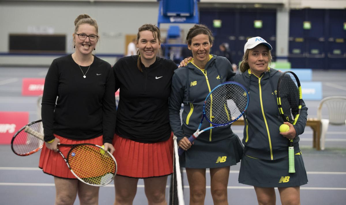four female tennis players stand at the net