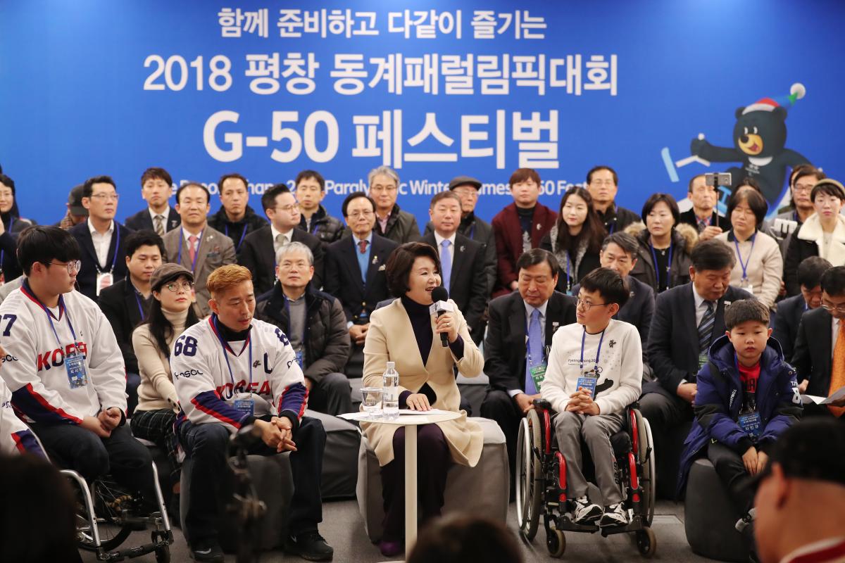 a woman speaks to a group of able bodied and wheelchair athletes