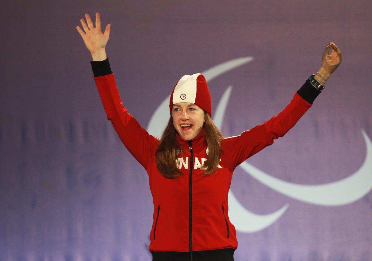 a female Para skier raises her arms in celebration on the podium