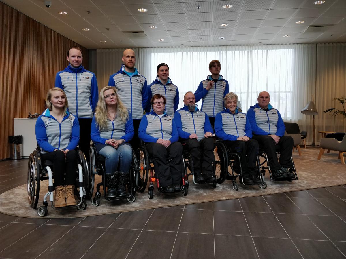 Four people standing behind a group of six people in wheelchairs