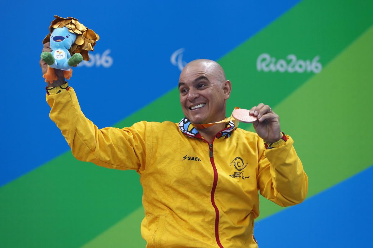 a male Para swimmer holds his bronze medal aloft