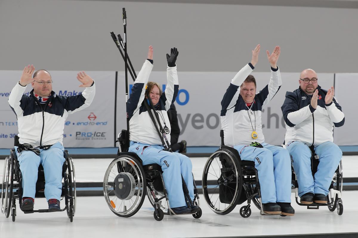 four wheelchair curlers raise their arms in celebration