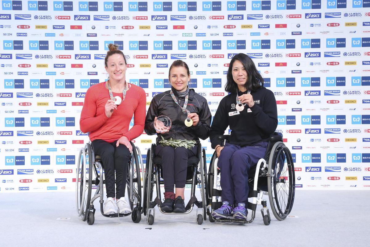 three female wheelchair racers on the podium with their medals