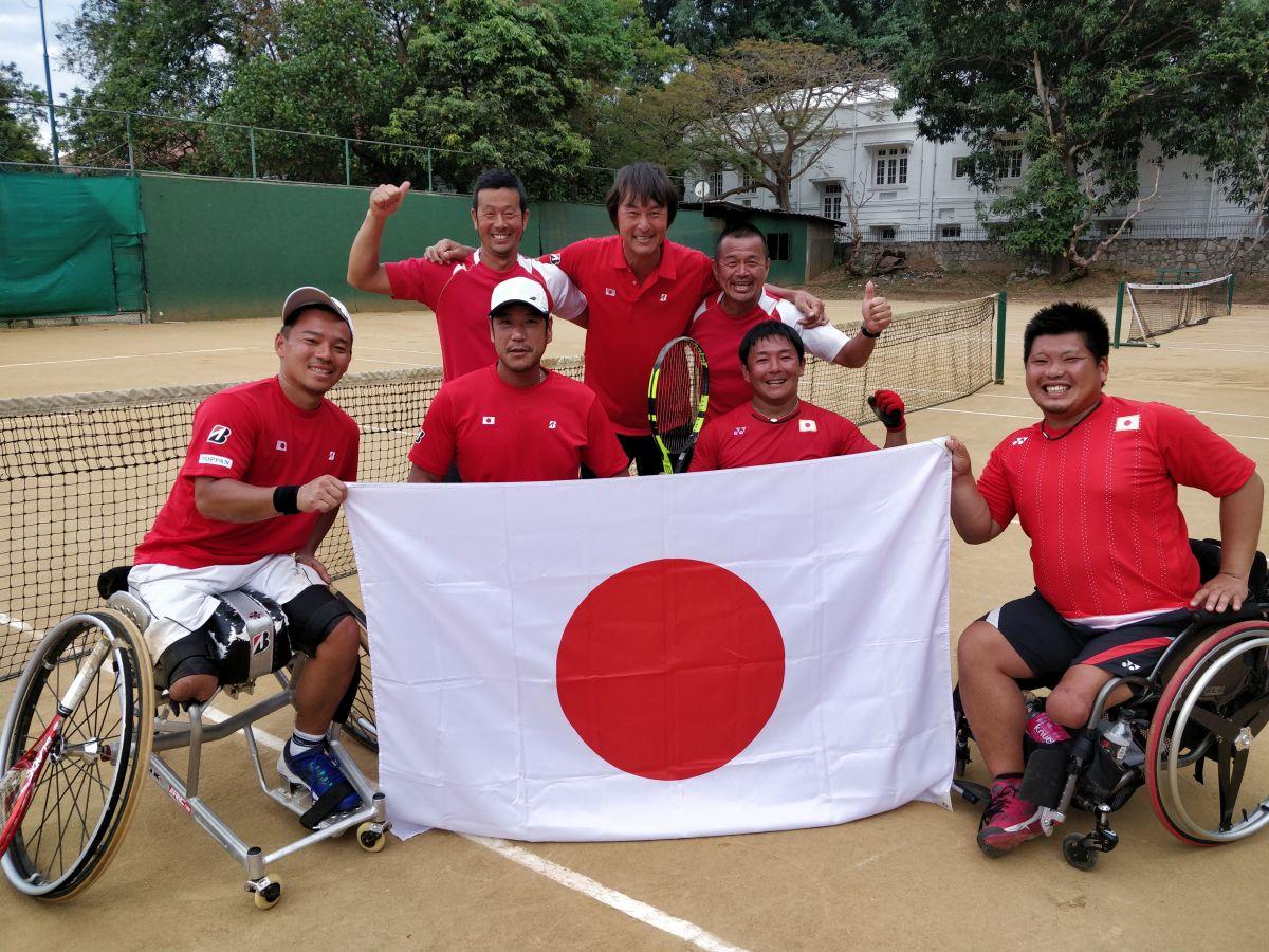 a group of male wheelchair tennis players pose with a Japanese flag