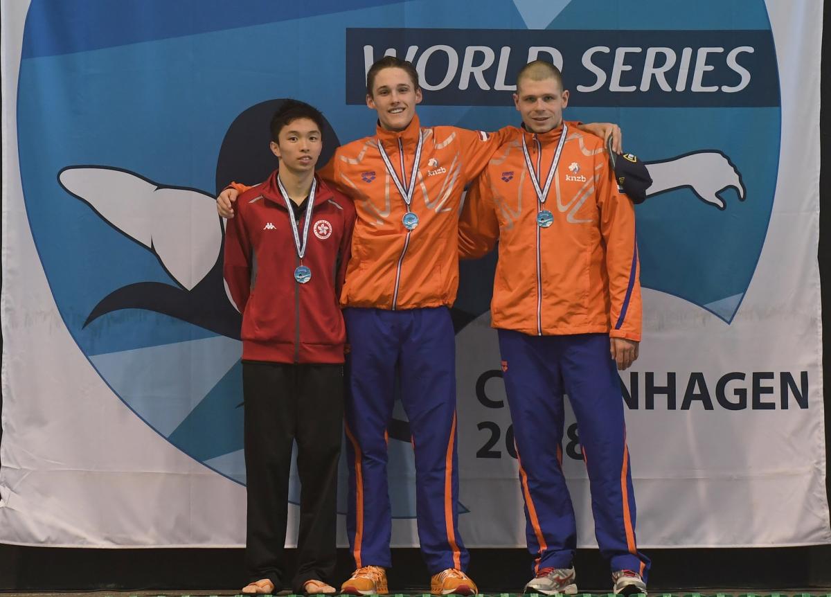 three male swimmers link arms on the podium