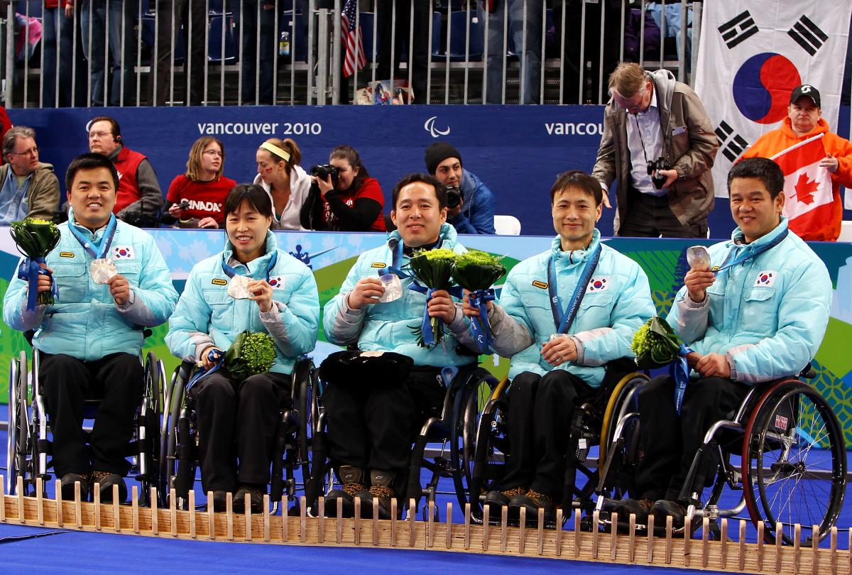 a group of wheelchair curlers celebrate on the podium