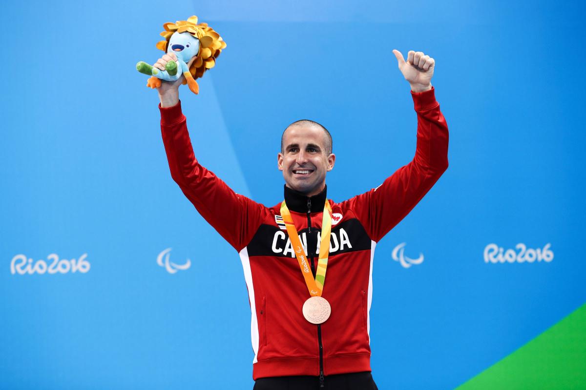 Benoit Huot a male Para swimmer raises his arms on the podium