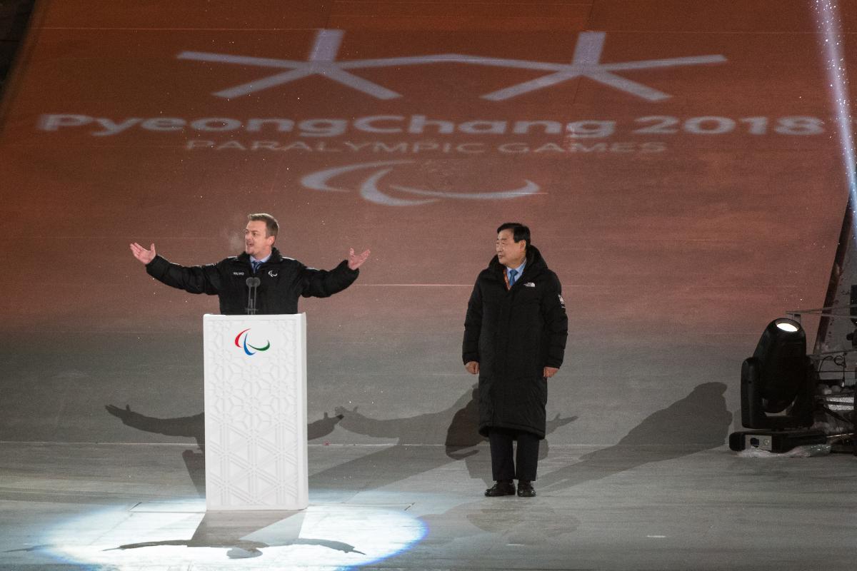 a man spreads his arms wide while speaking at a podium