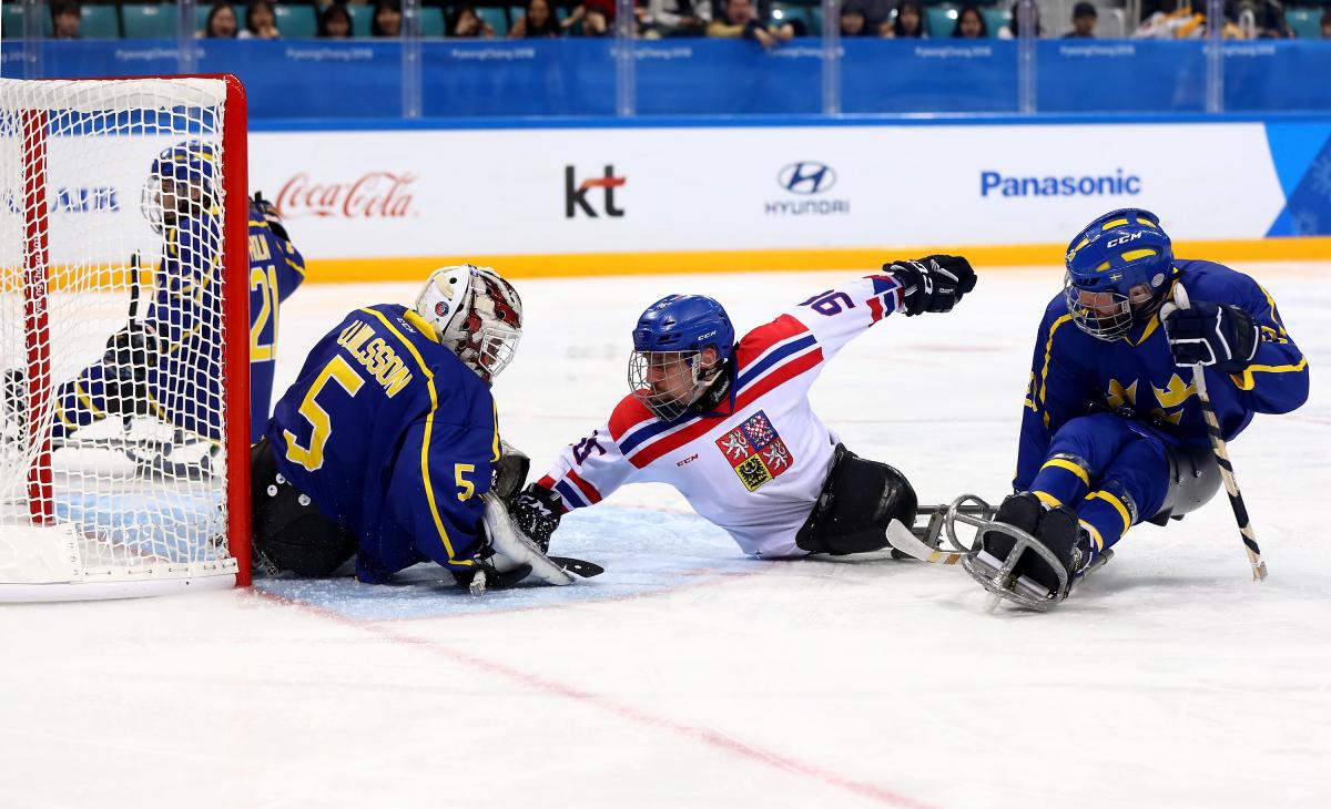 three ice hockey players clash in front of goal