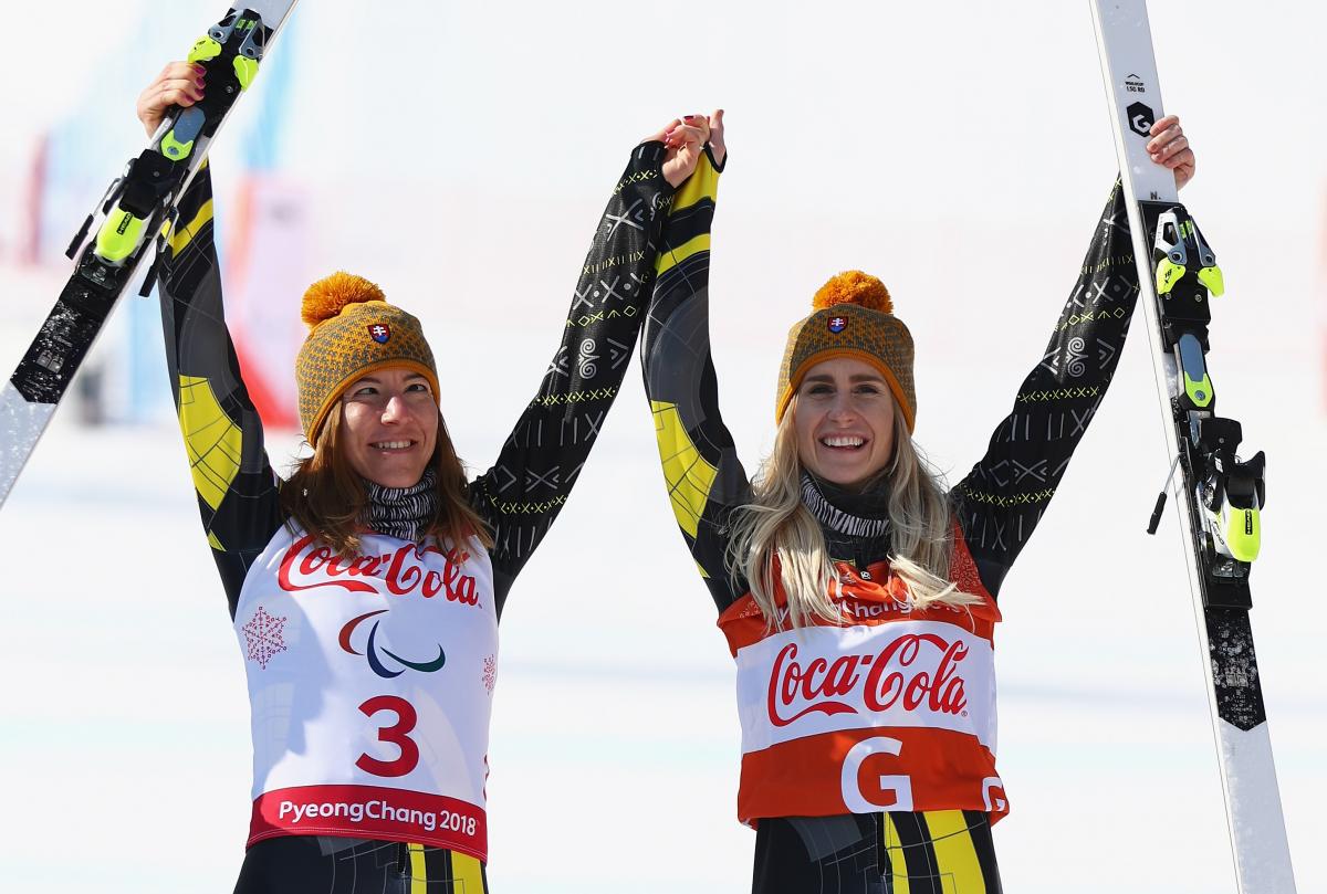 a female vision impaired skier and her guide raise their arms in celebration