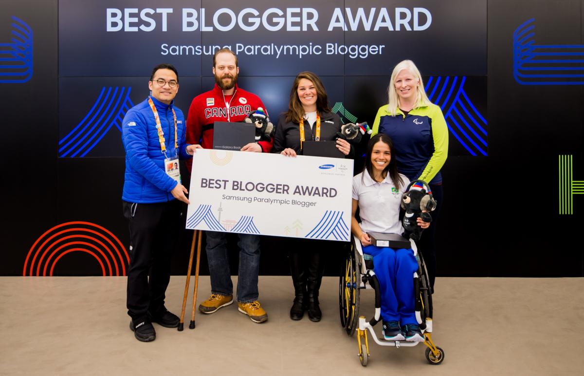 five people standing in front of a video screen