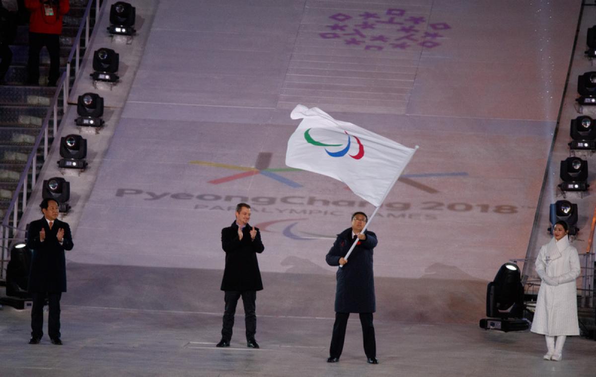 Three men standing, one of them holding a flag