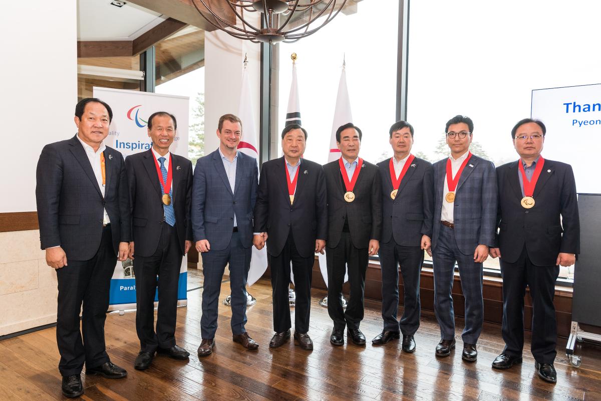 Eight men standing, six of them with the Paralympic Order medal 