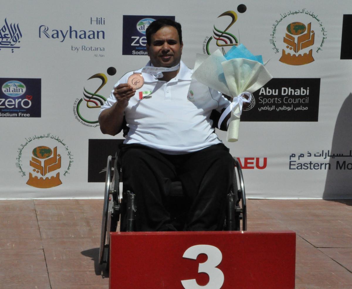 Man in wheelchair holding medal and flowers