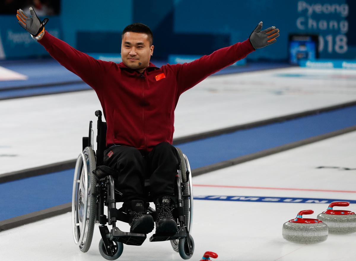 a male wheelchair curler raises his arms in celebration