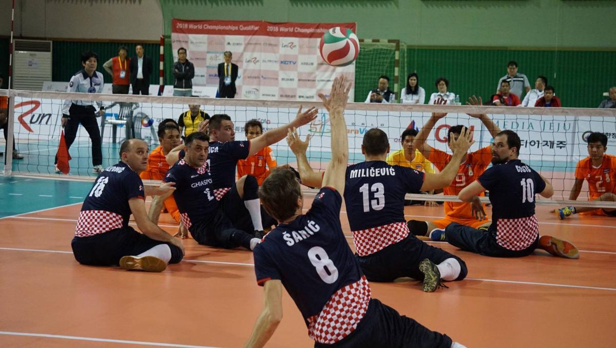 a group of male sitting volleyball players in action on the court