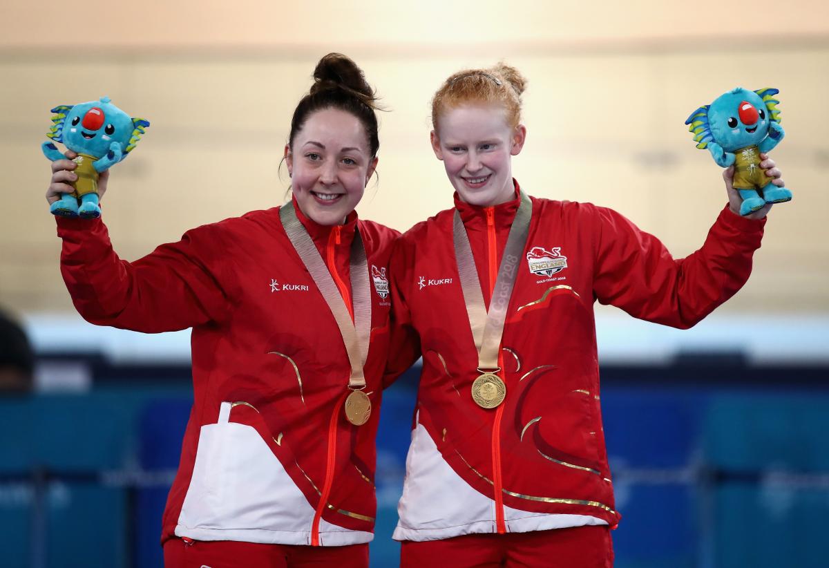 two female Para cyclists stand on the podium with their gold medals