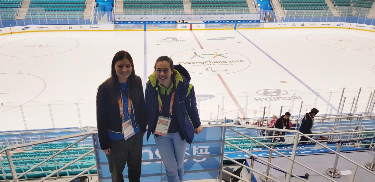 two women stand looking down at an ice hockey rink