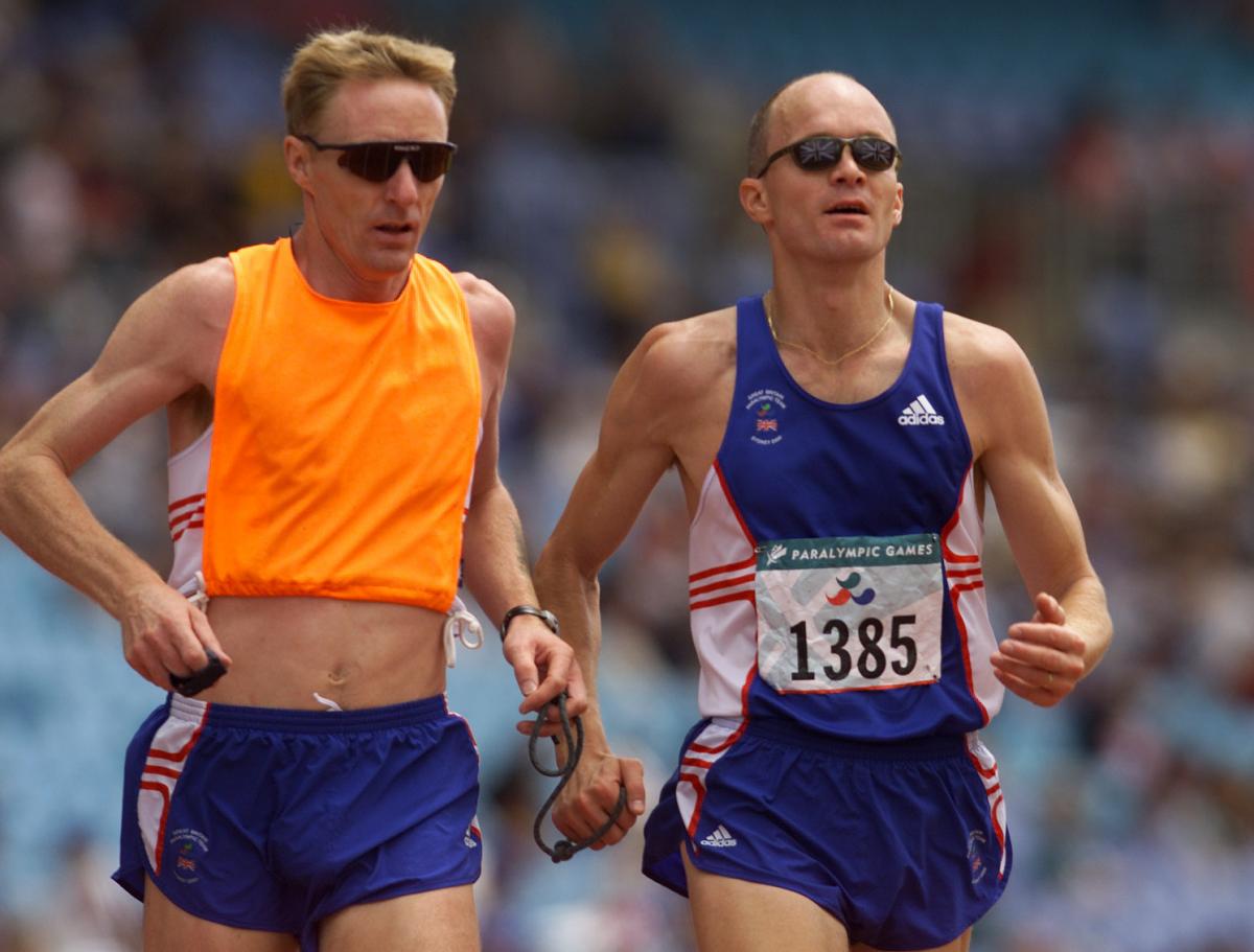 a male vision impaired runner and his guide during a race