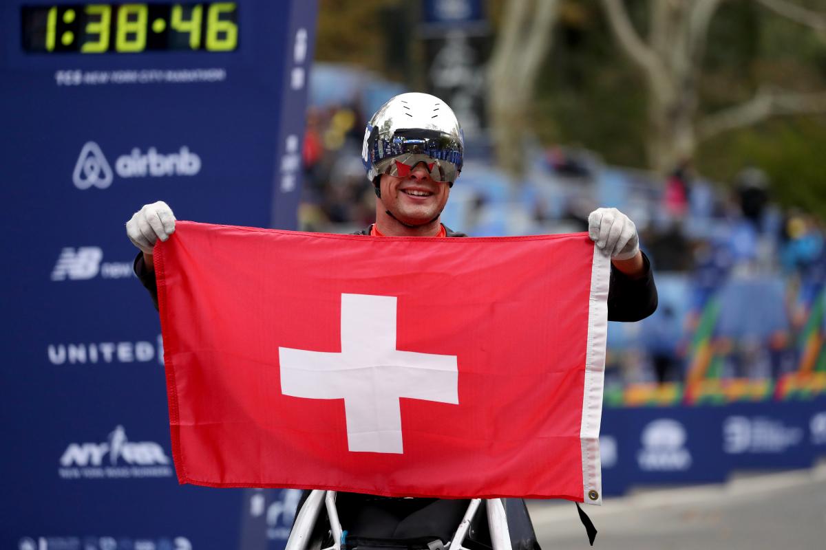 a male wheelchair racer holds up the Swiss flag