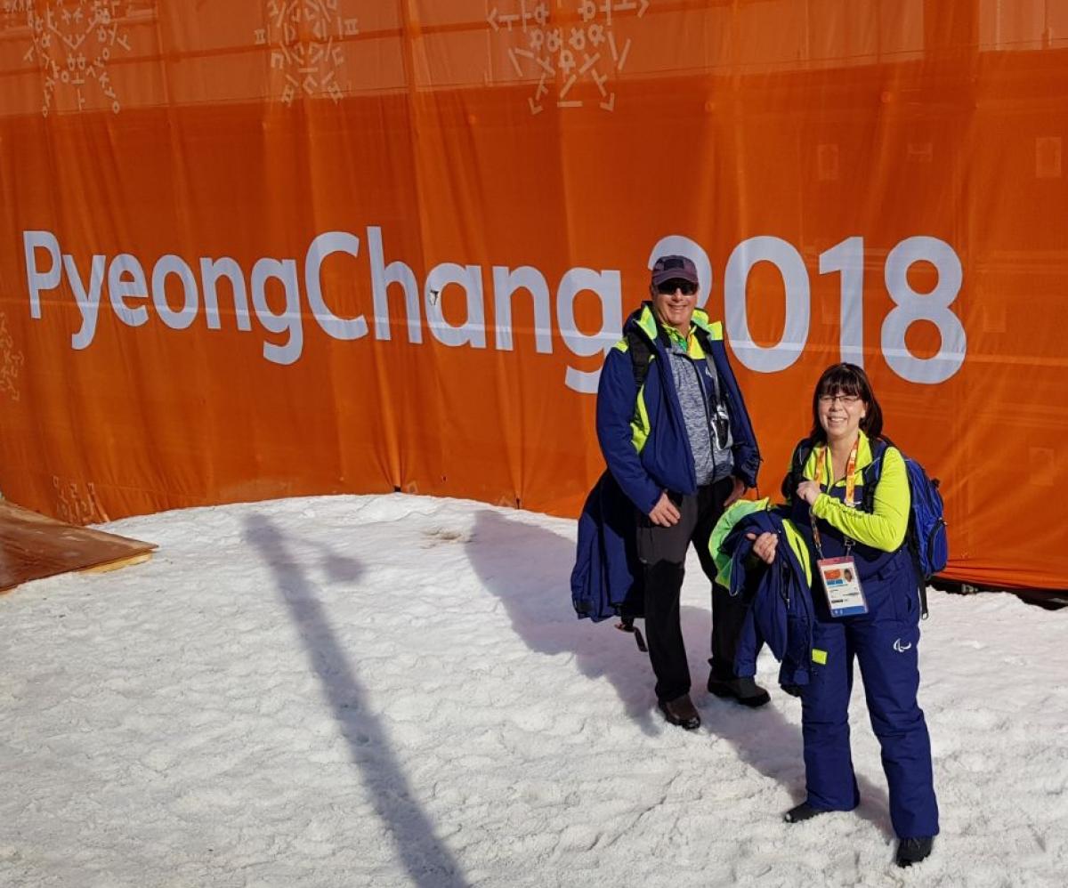 Angela Schornstein - alpine skiing and snowboard official Two winter sport officials pose in front of a PyeongChang 2018 banner