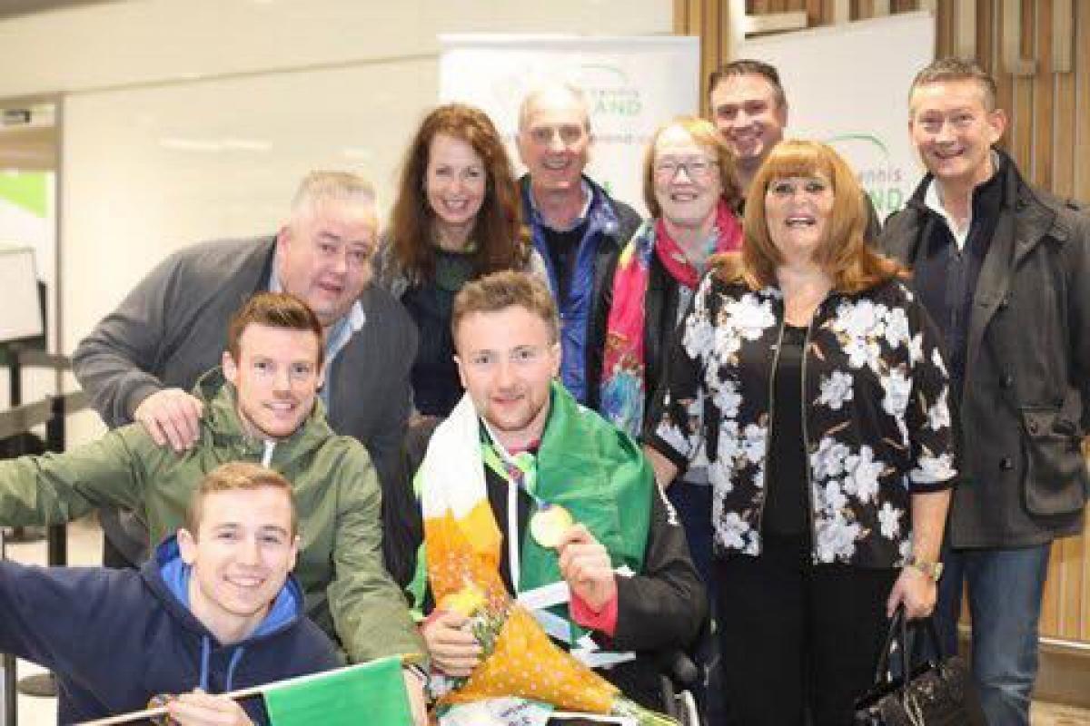 Man in wheelchair with Irish flag around him and his family