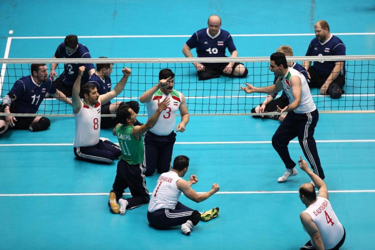 a group of male sitting volleyball players celebrate on the court