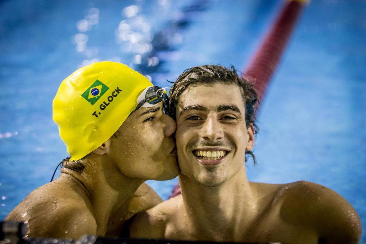 one male swimmer kissing another on the cheek in celebration