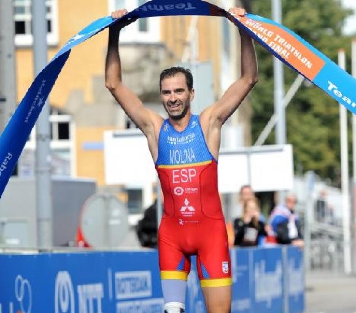 Daniel Molina a male Para triathlete holds up the finish line tape as he crosses