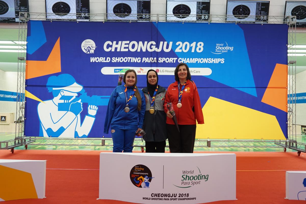 Three female shooting athletes pose on the podium